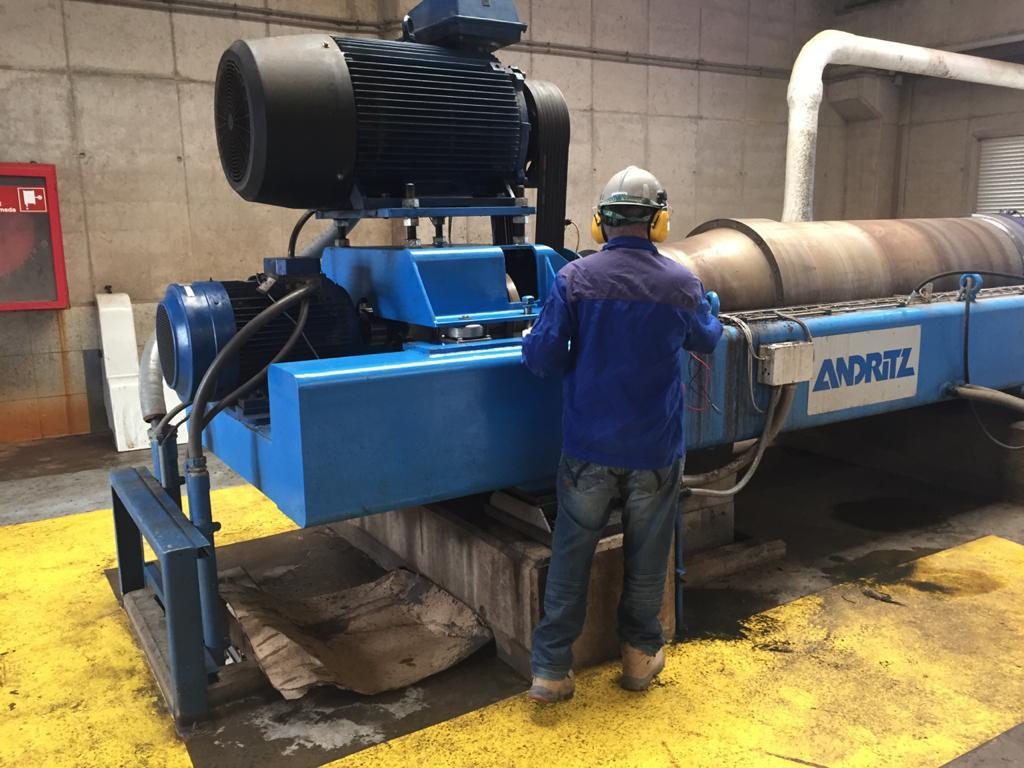 Técnico de Filtramec con casco y protección auditiva trabajando junto a una centrífuga decanter en planta.